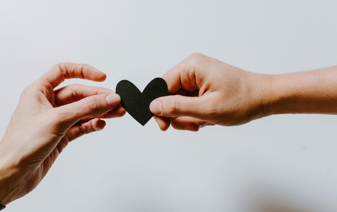 Two hands, each holding a side of a cut out black paper heart