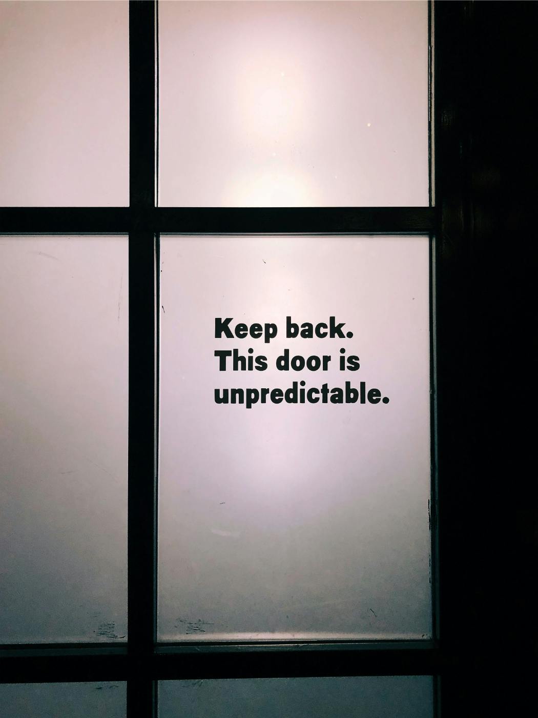 A door with glass panels on one planet is written: Keep Back This Door Is Unpredictable