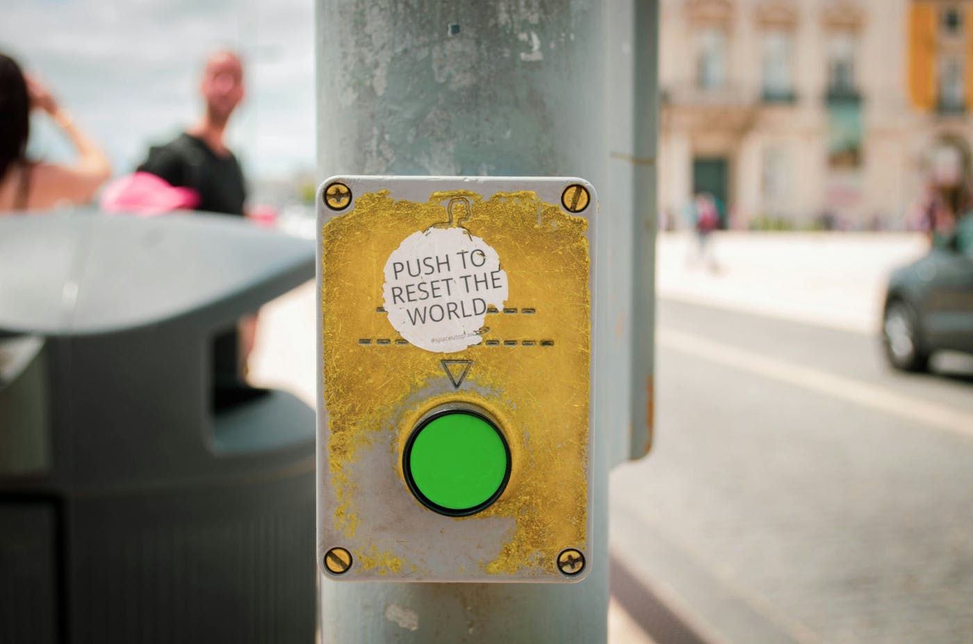 A green button to cross the street with a sticker over it reading Push to Reset the World