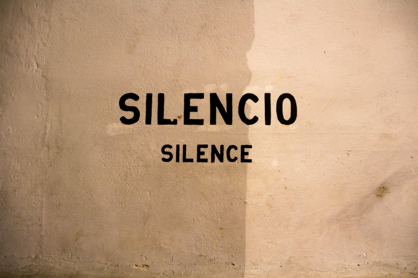 Words reading SILENCIO and under it SILENCE stenciled on a tan wall