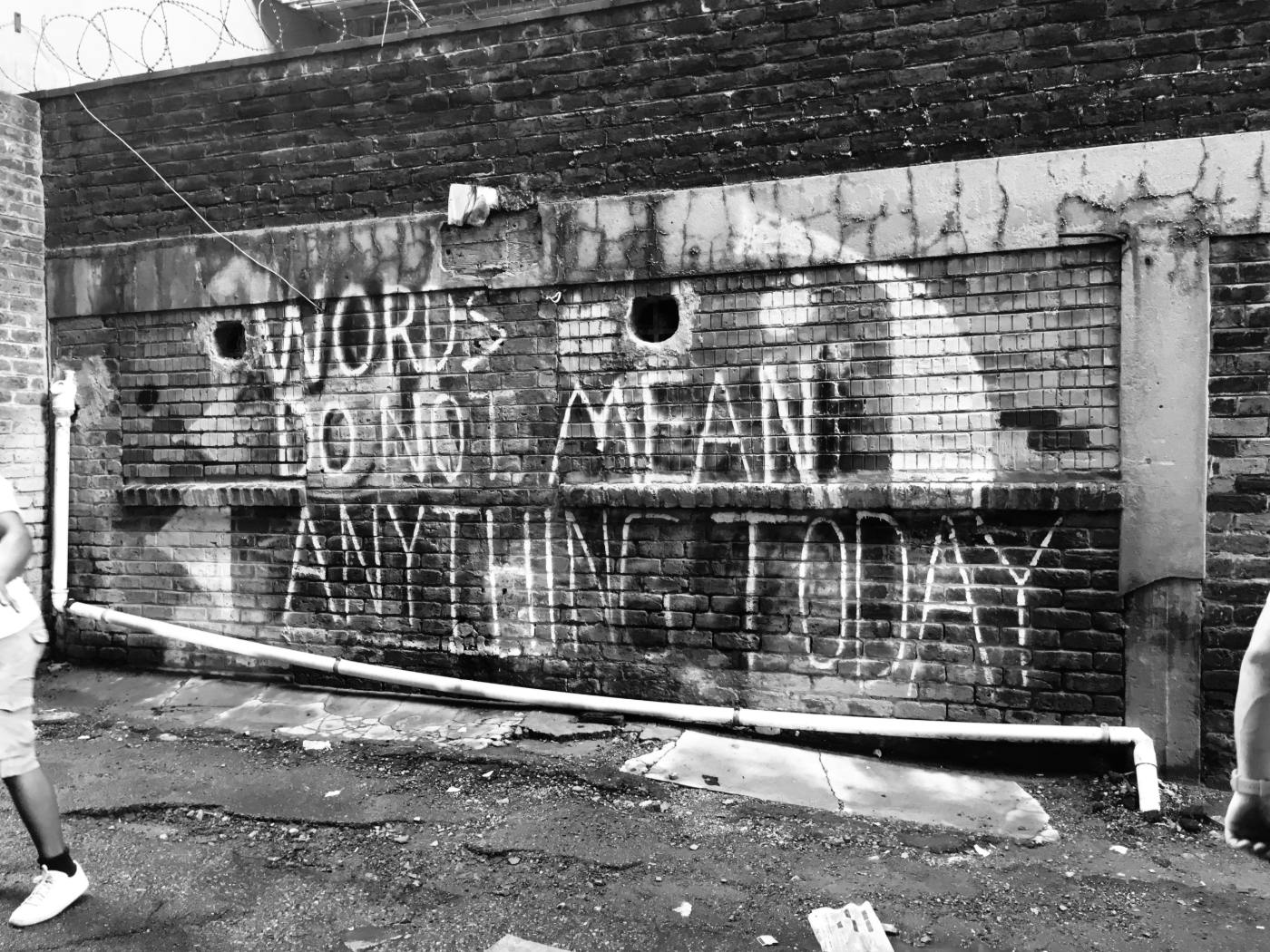 A gray scale image of a brick wall with graffiti reading: Words Do Not Mean Anything Today