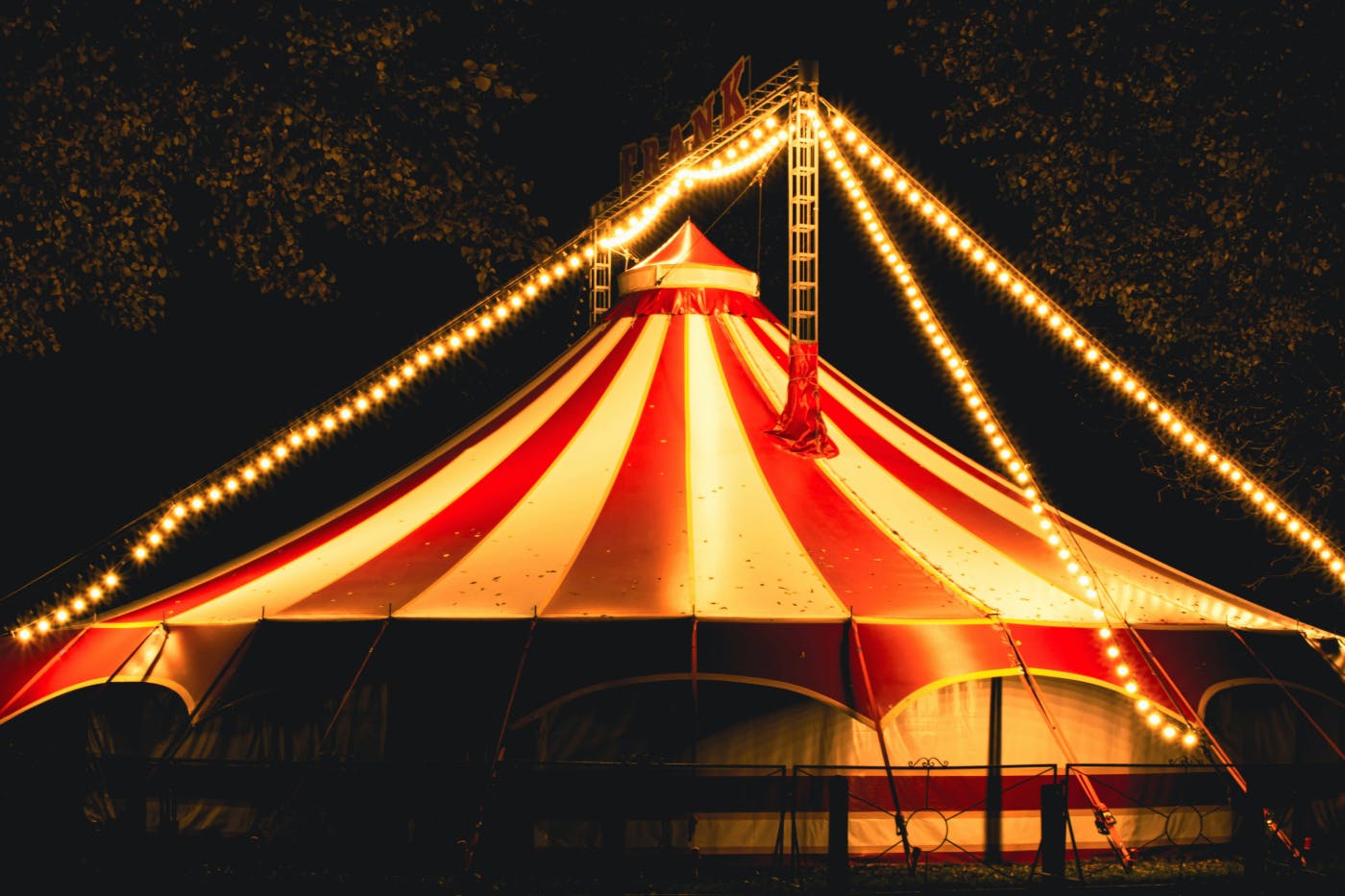 A large red and white circus tent with strings of lights
