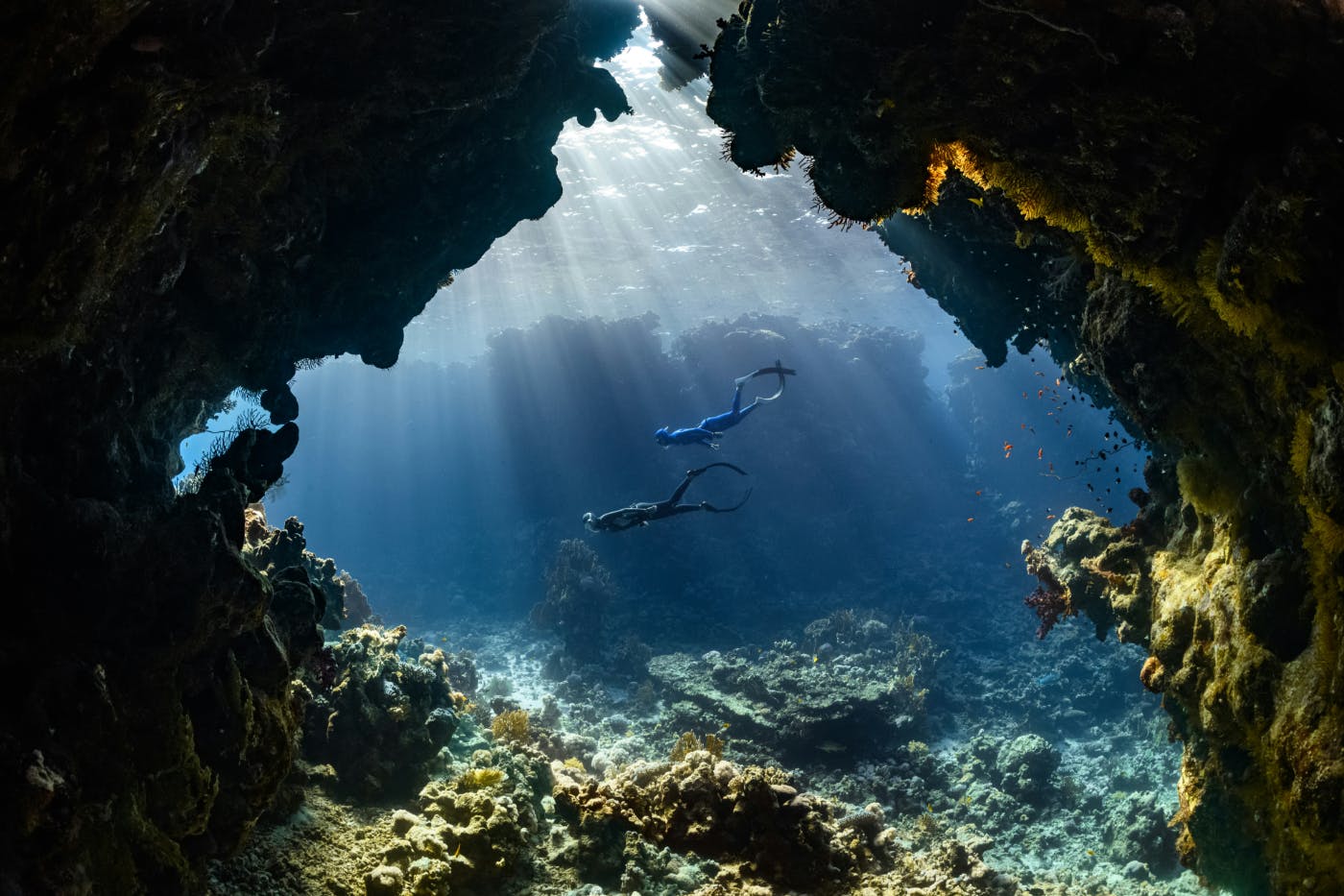 Two divers swimming through an underwater cave