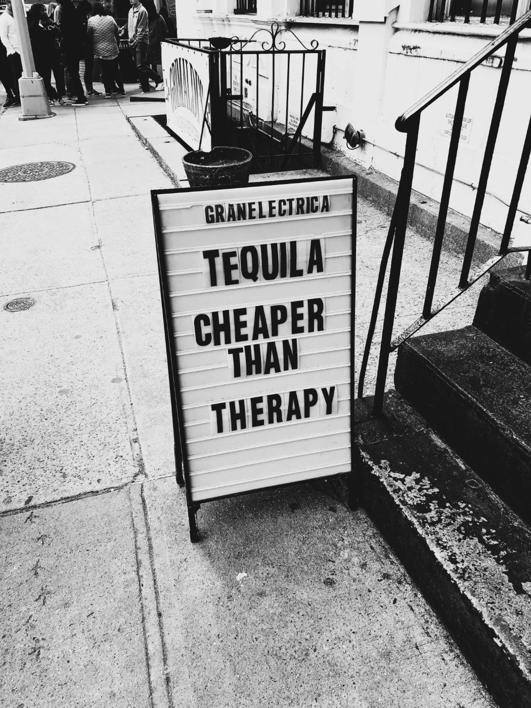 A black and white of a street sign reading Tequila Cheaper than Therapy