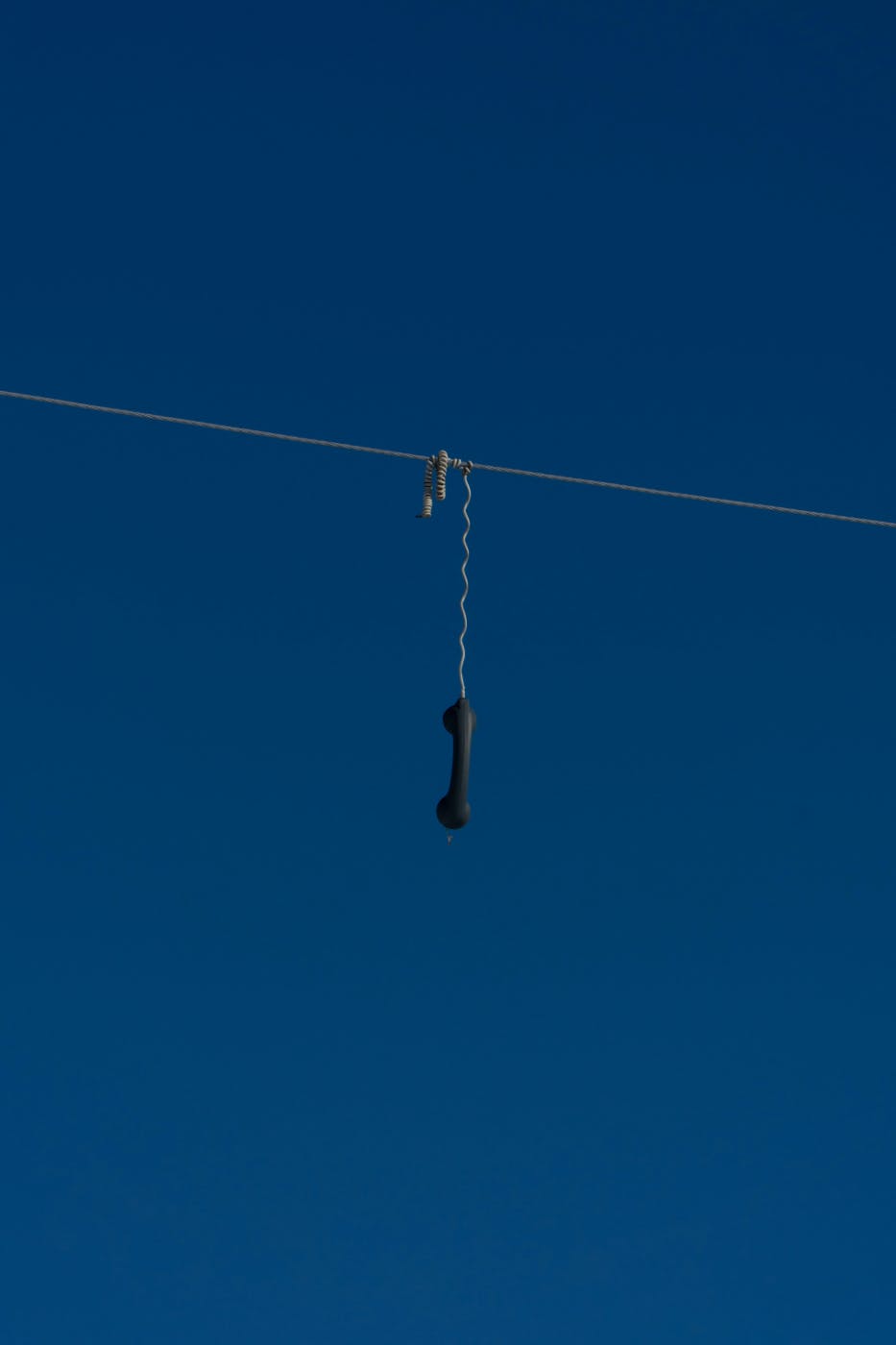 The handset of a phone with a cord hanging over a telephone wire