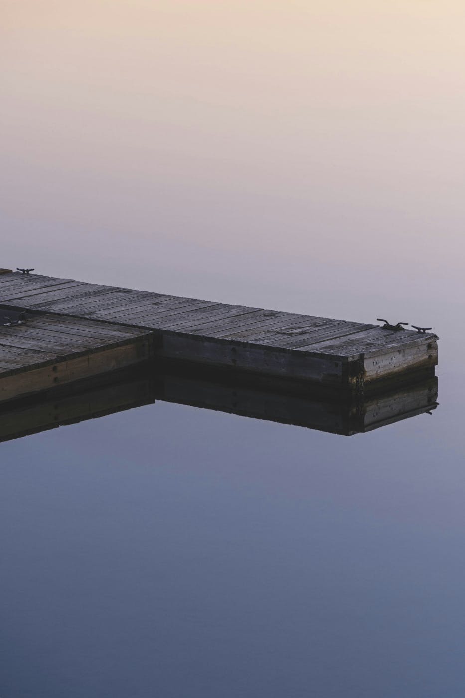 A wooden dock on a dead calm lake at dusk
