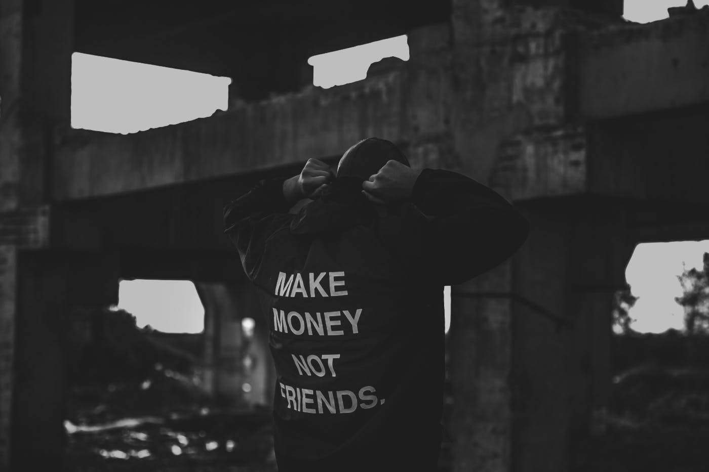 A black and white shot of a guy in a parking garage wearing a sweatshirt with Make Money Not Friends on the back