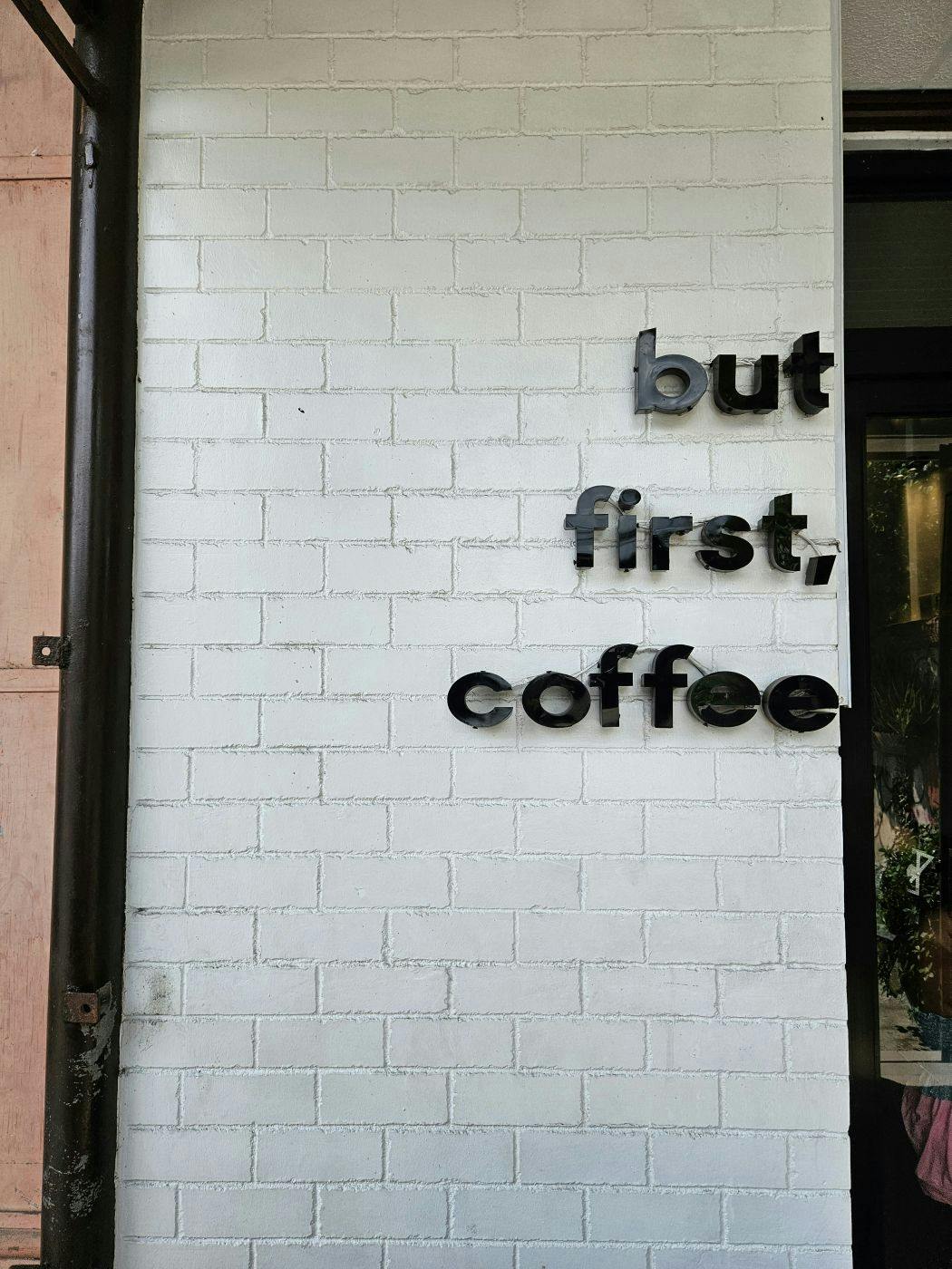 A white brick wall with But First Coffee in black letters