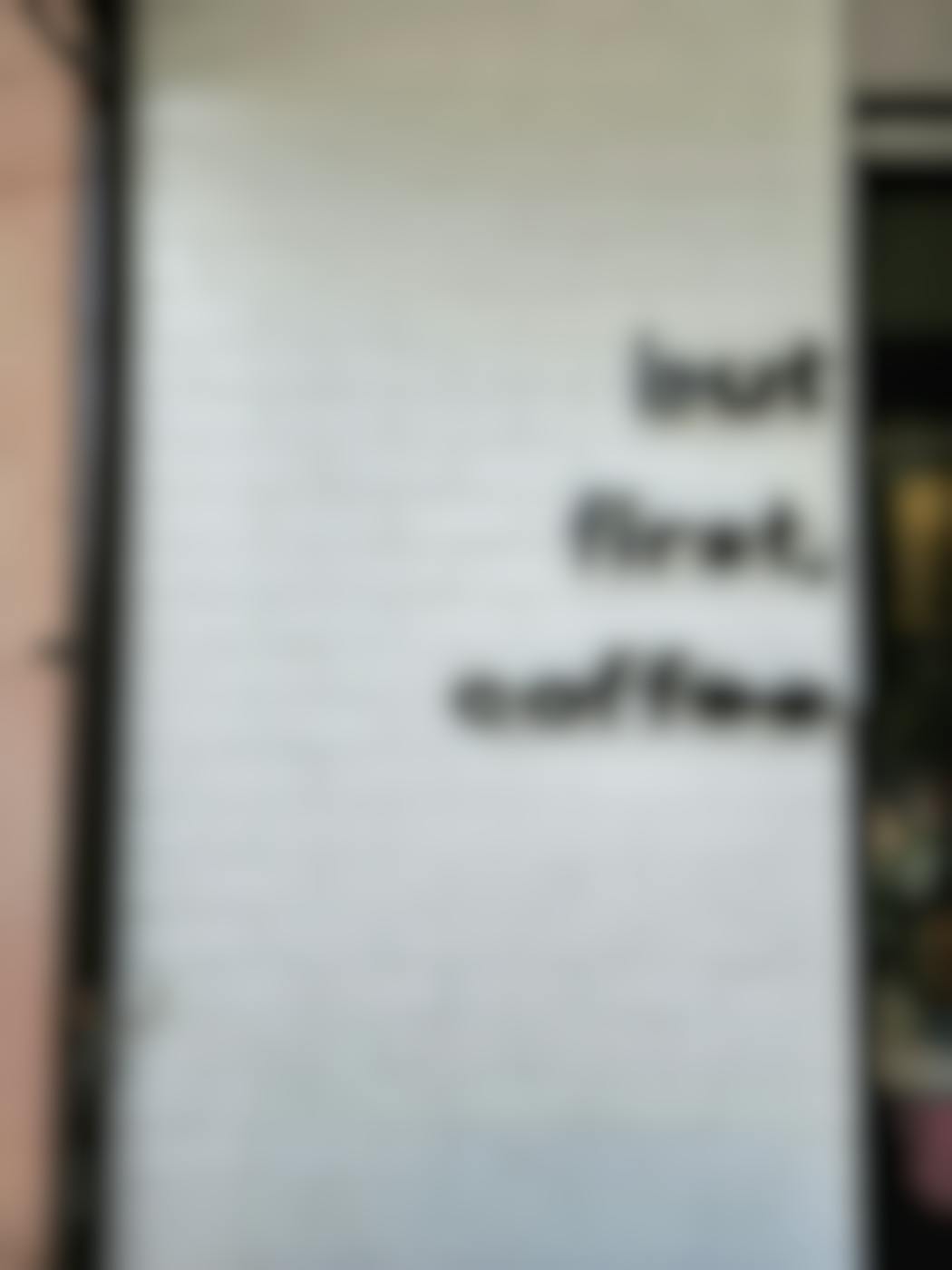 A white brick wall with But First Coffee in black letters