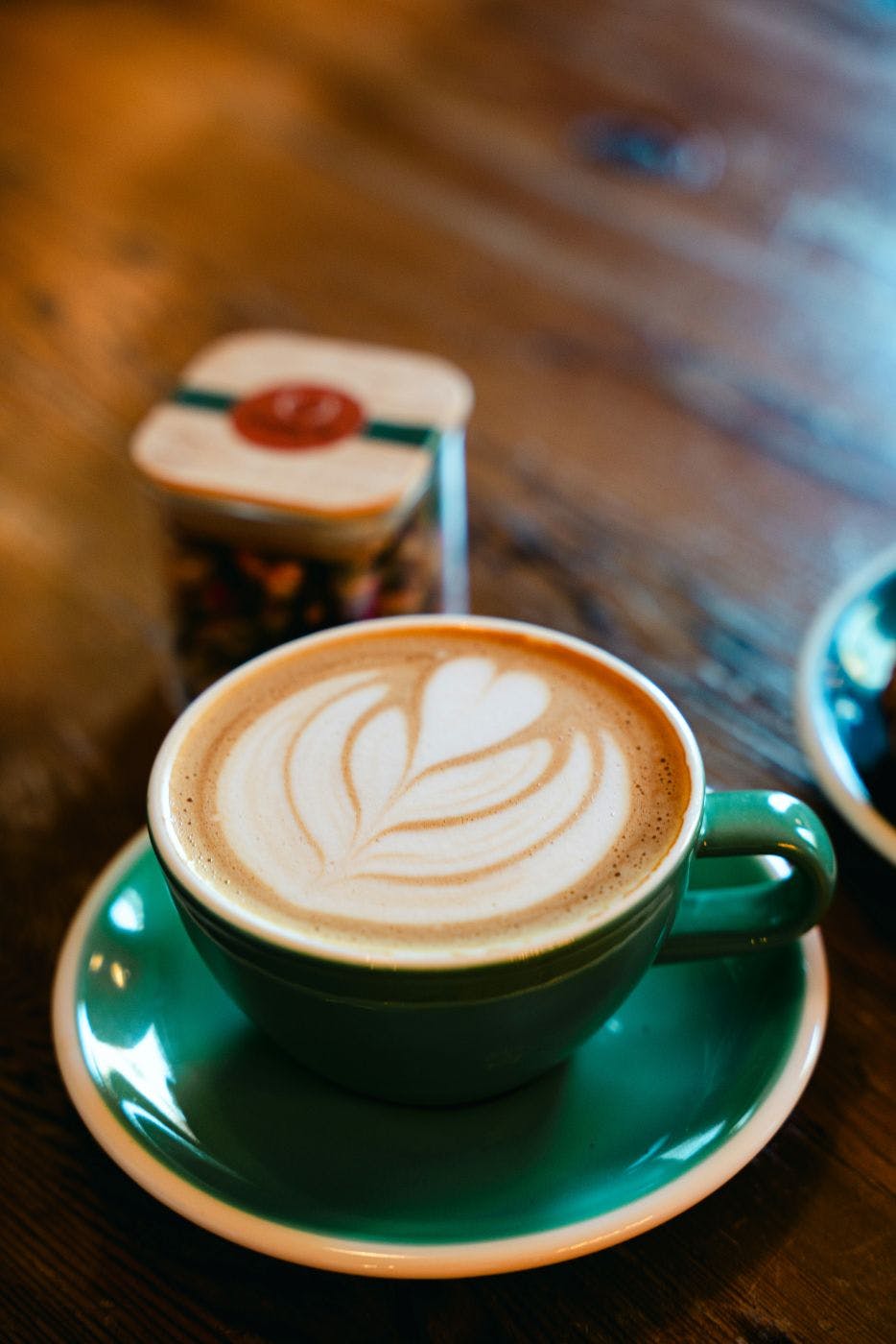 A latte in a green cup with a flower made in the foam