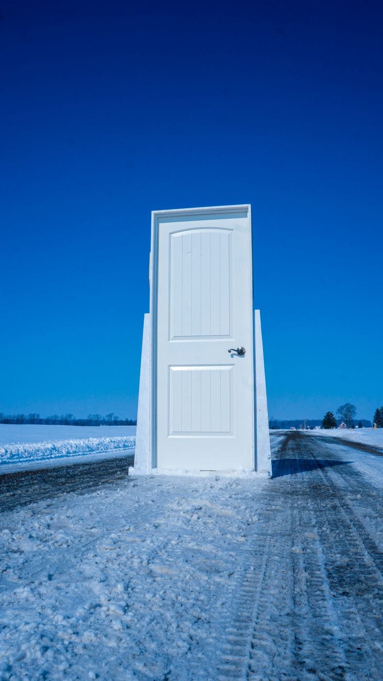 A white door and jamb in the middle of a snowy road