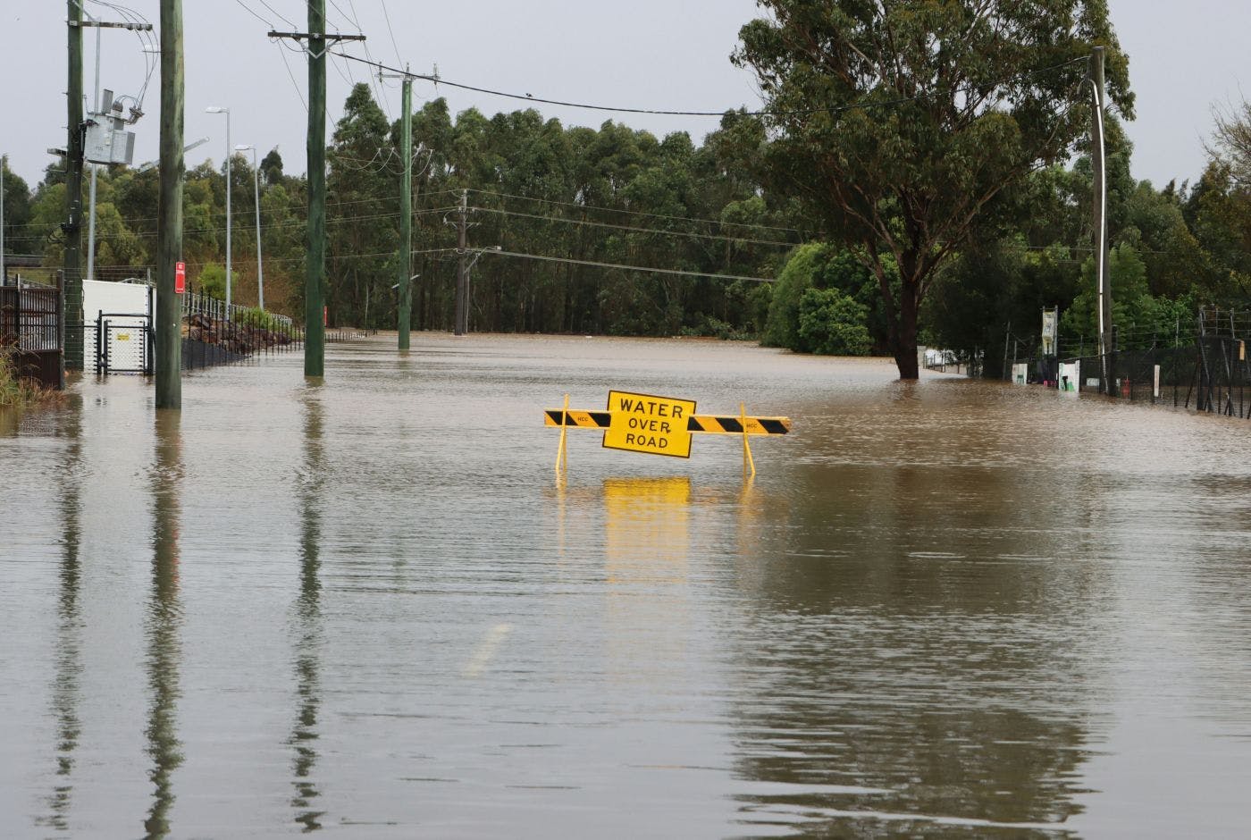 A flooded street with a yellow sign on a black and yellow barrier reading Water Over Road