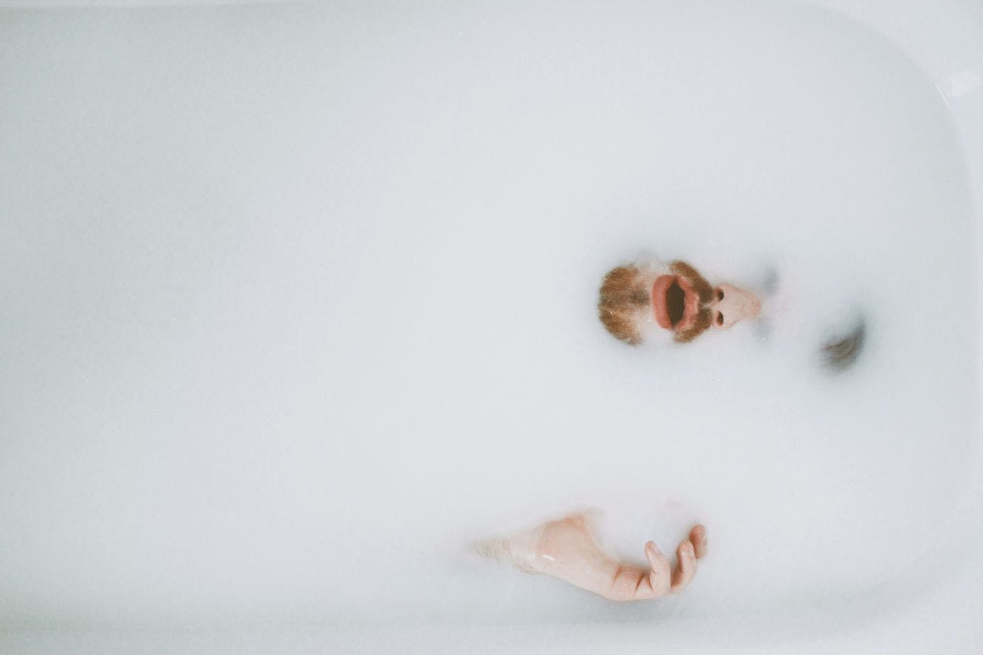 A bearded man almost completely submersed in a cloudy bath
