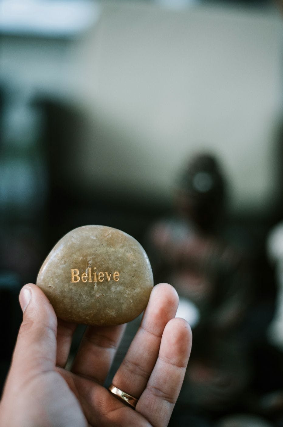 A hand holding a stone with the word Believe craved in it