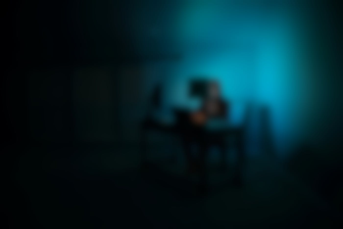 Someone in a mask behind a computer, room lit by blue computer light