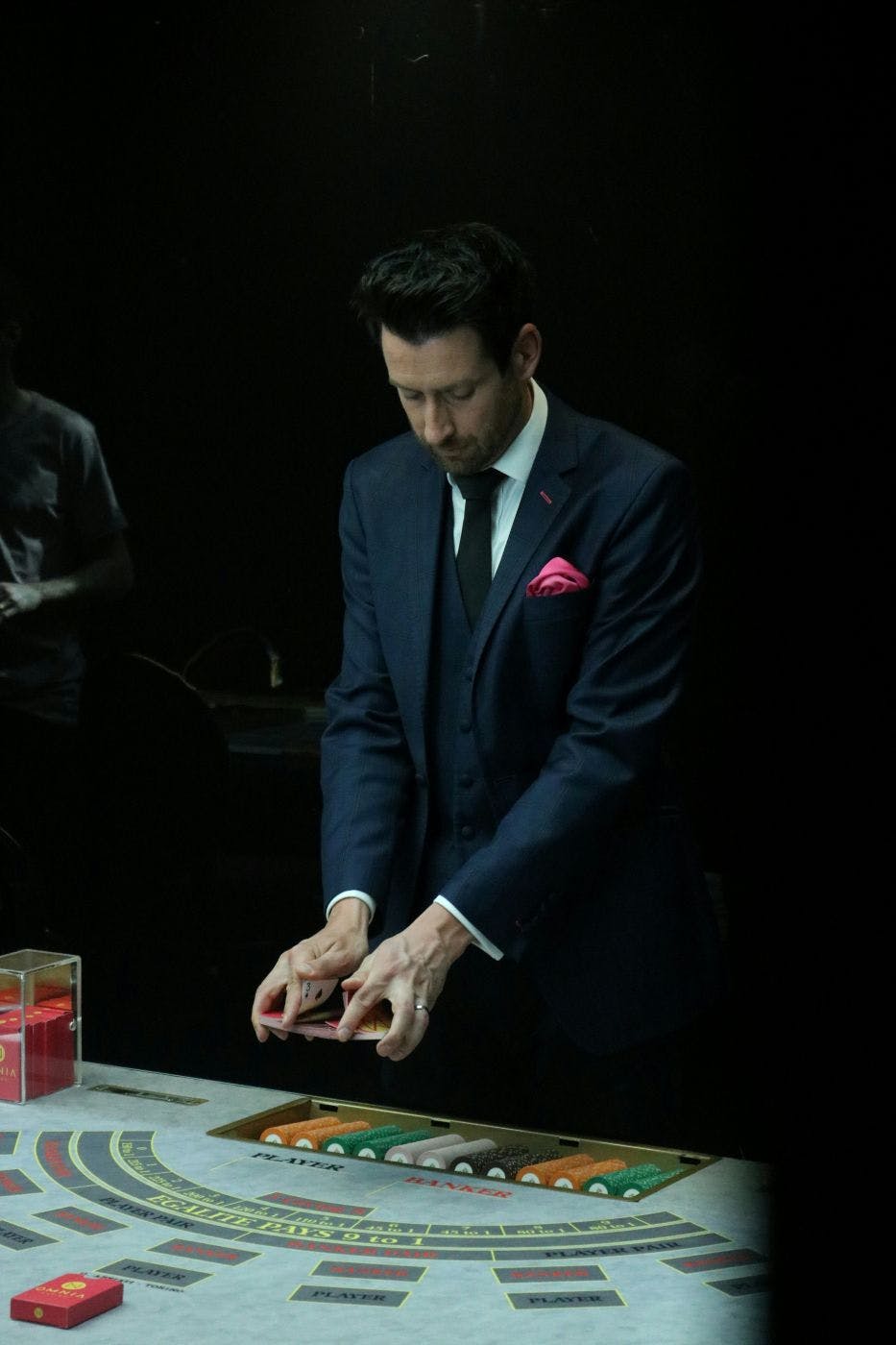 A man in a three-piece suit shuffling a deck of cards over a blackjack table