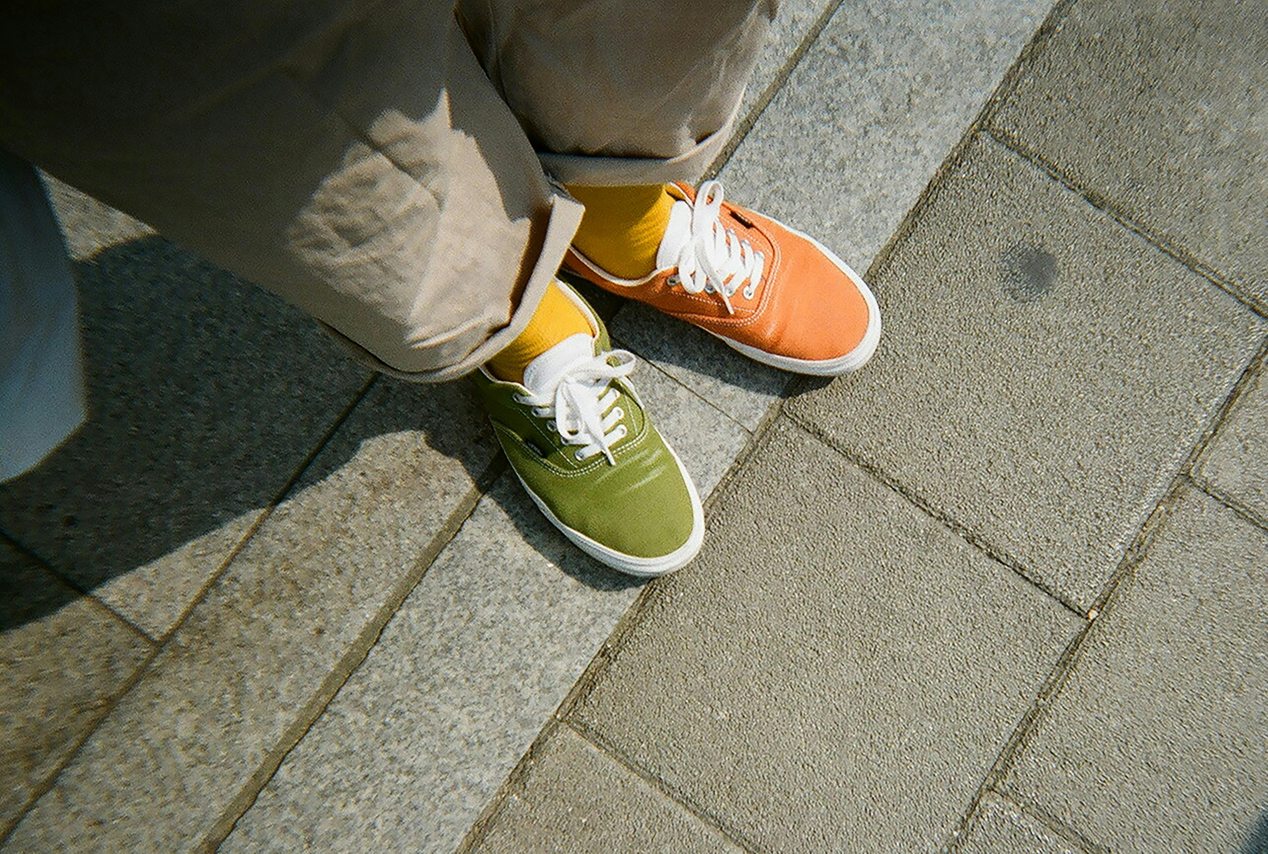 A person wearing one orange and one green sneaker