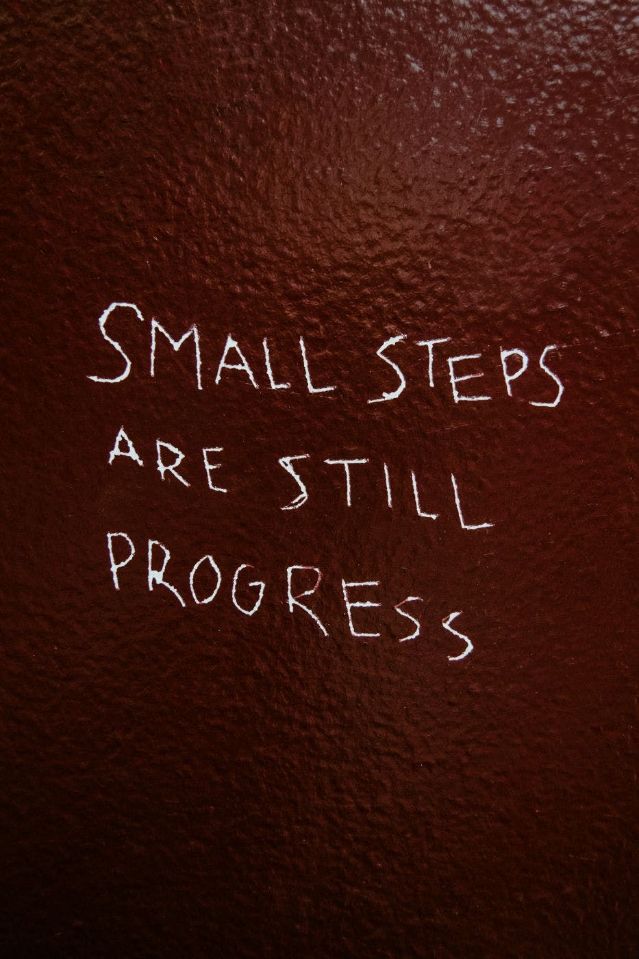 A red wall with Small Steps are Still Progress scratched on it