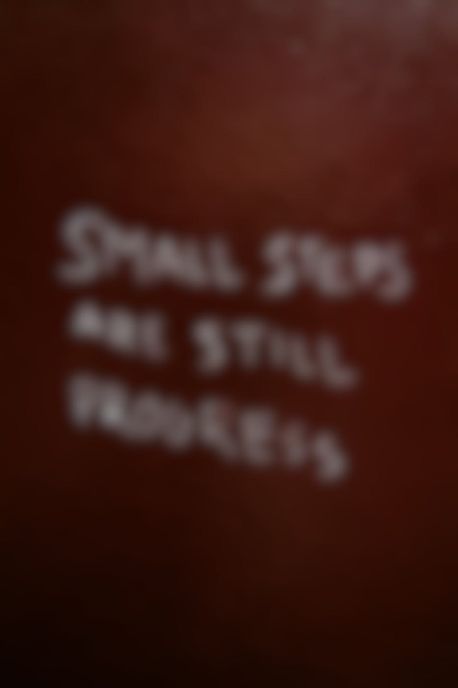 A red wall with Small Steps are Still Progress scratched on it
