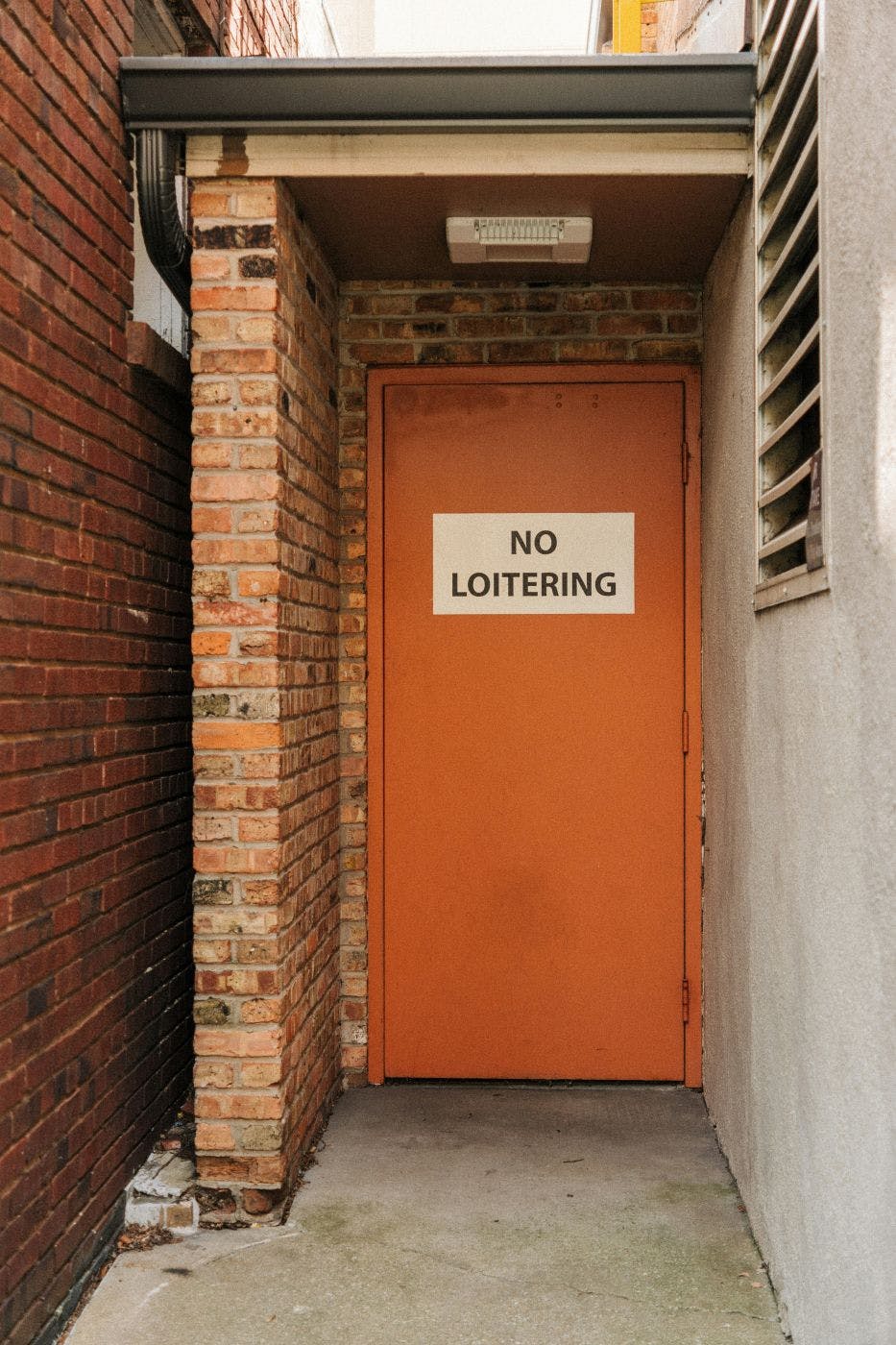 A small alley with an orange door with a No Loitering sign on it