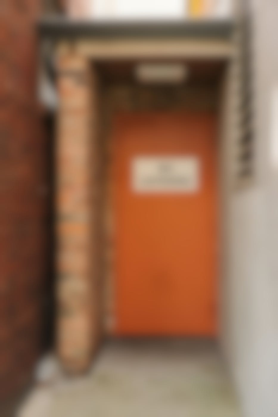 A small alley with an orange door with a No Loitering sign on it