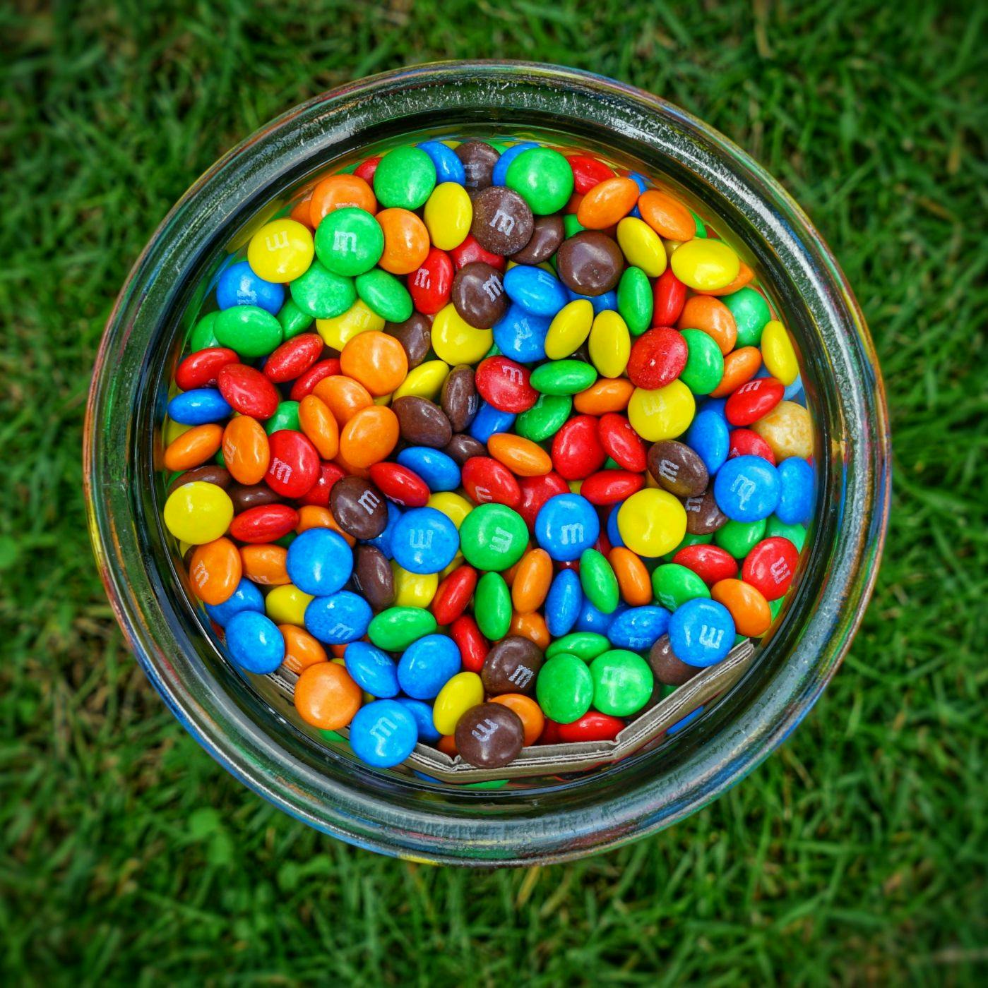 Top view of a jar full of M&Ms on grass