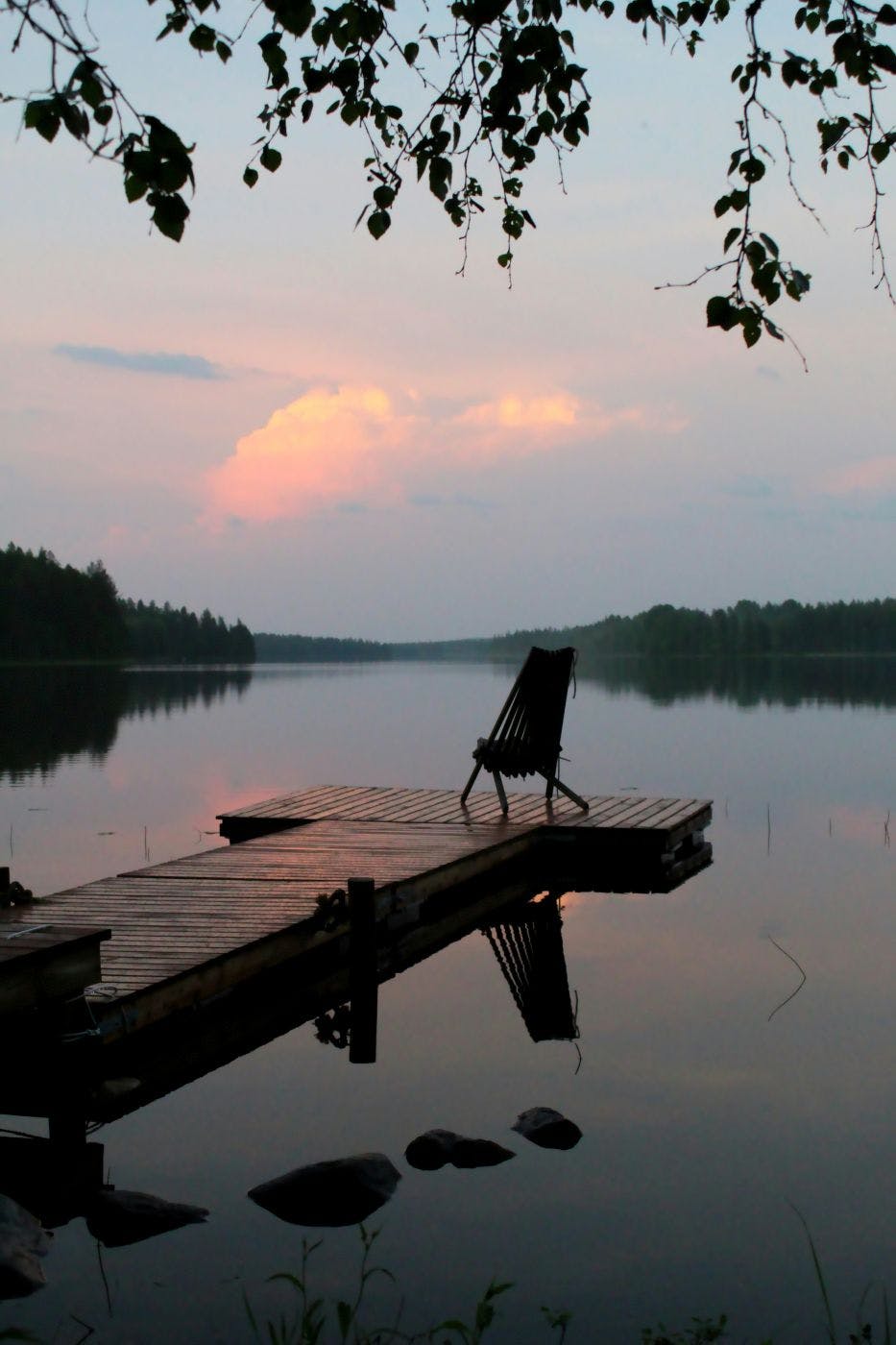 A chair at the end of a wooden dock on a still lake