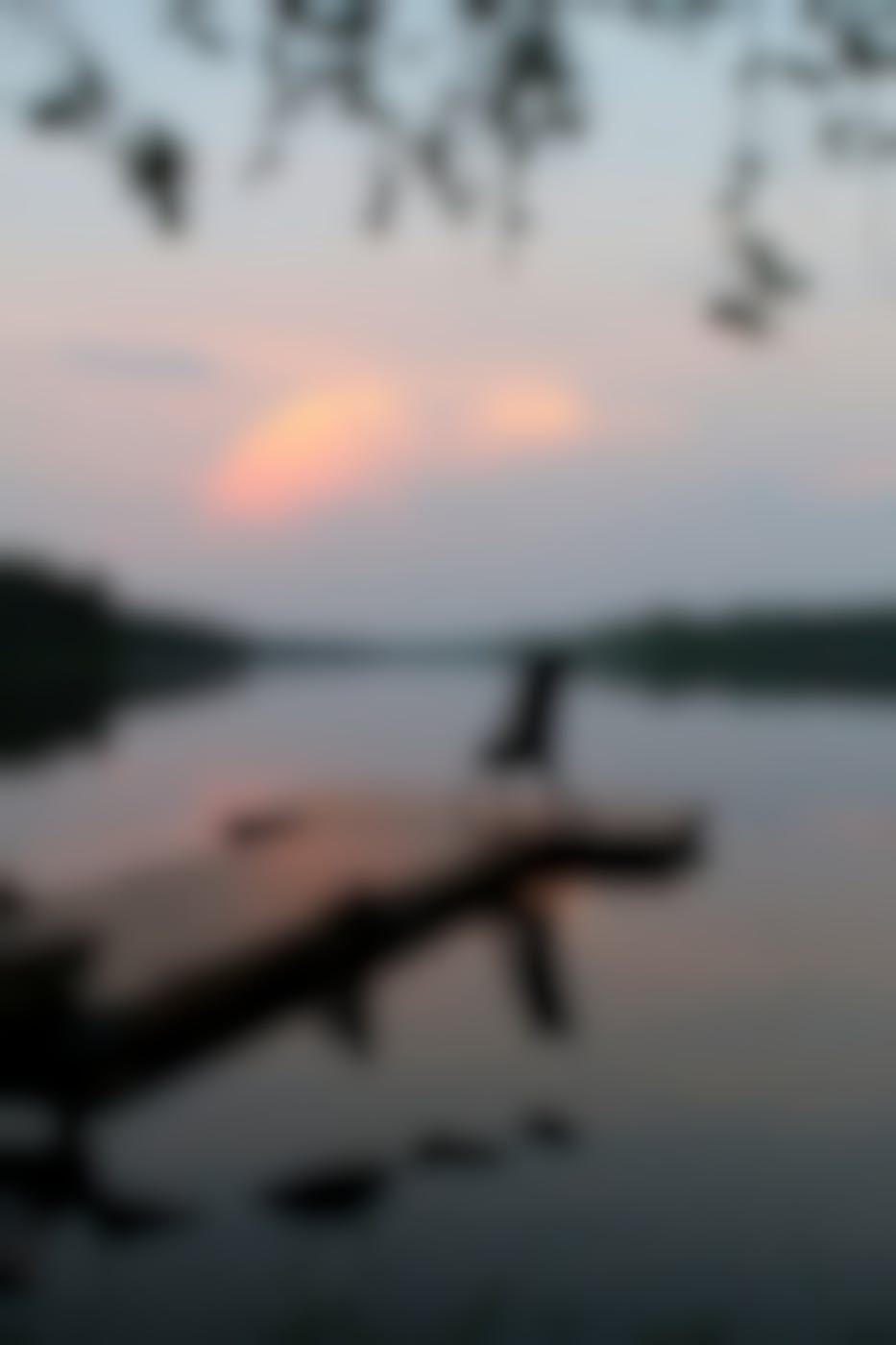 A chair at the end of a wooden dock on a still lake