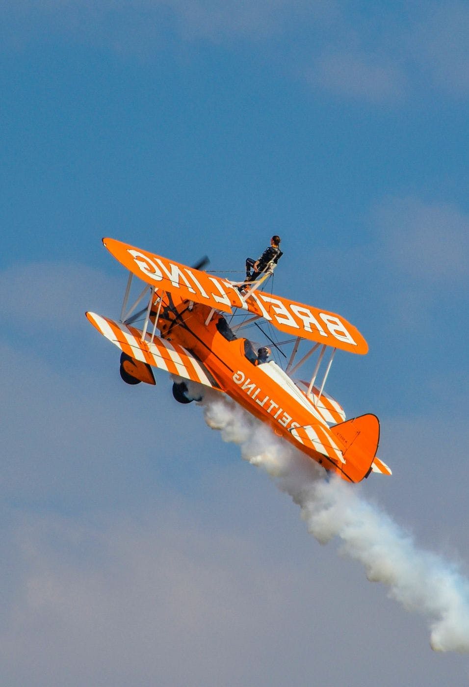 A wing walker on an orange and yellow biplane