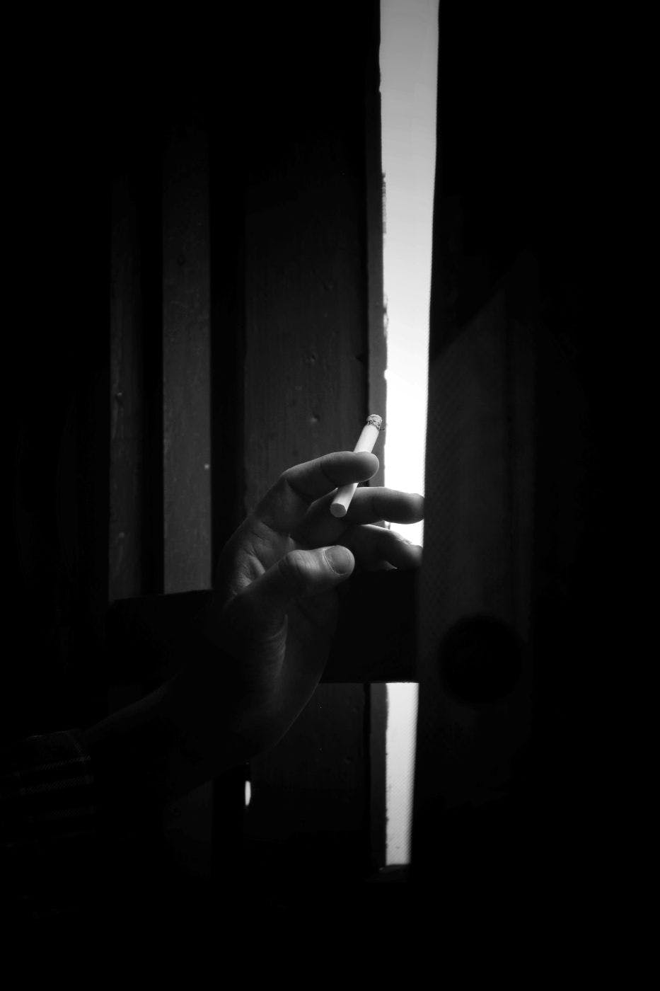 A hand holding a cigarette opening a curtain slightly