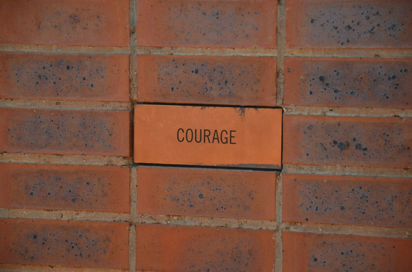 An old brick wall with one newer brick that has the word courage carved into it