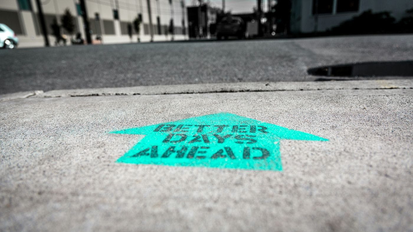 A teal arrow stenciled on the street with the words Better Day Ahead