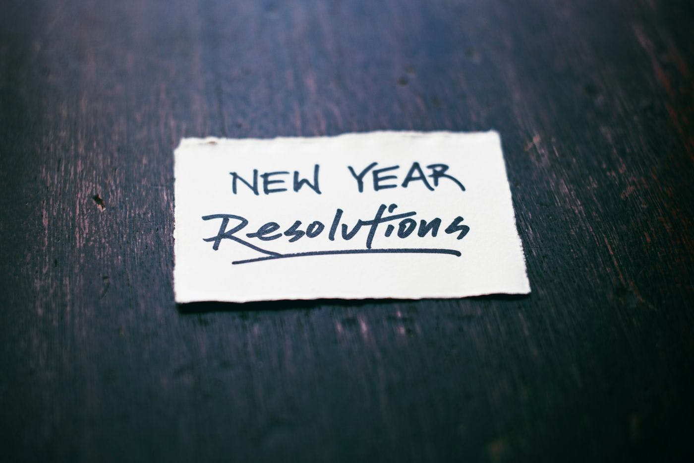 A white bit of paper with New Year Resolutions written on it, sitting on a black table