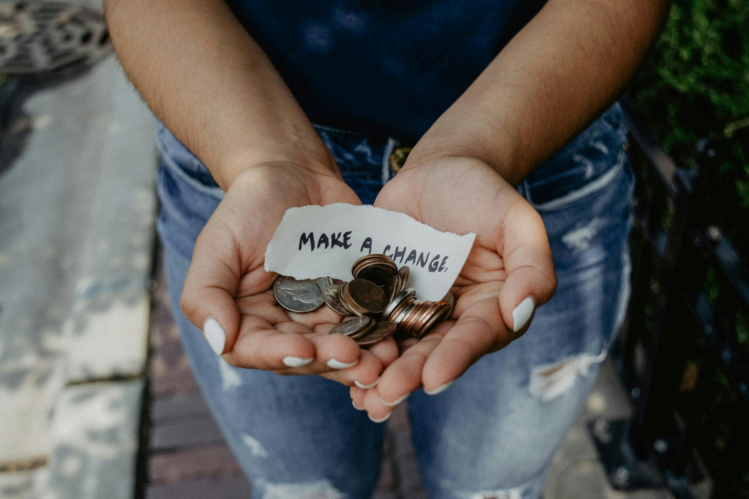 A woman's hands holding some change and a small sign reading make a chiange