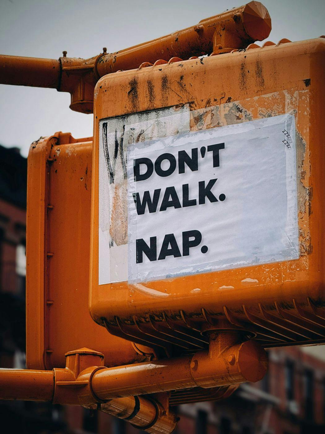 orange traffic signal with a sheet of paper on it reading Don't Walk. Nap.