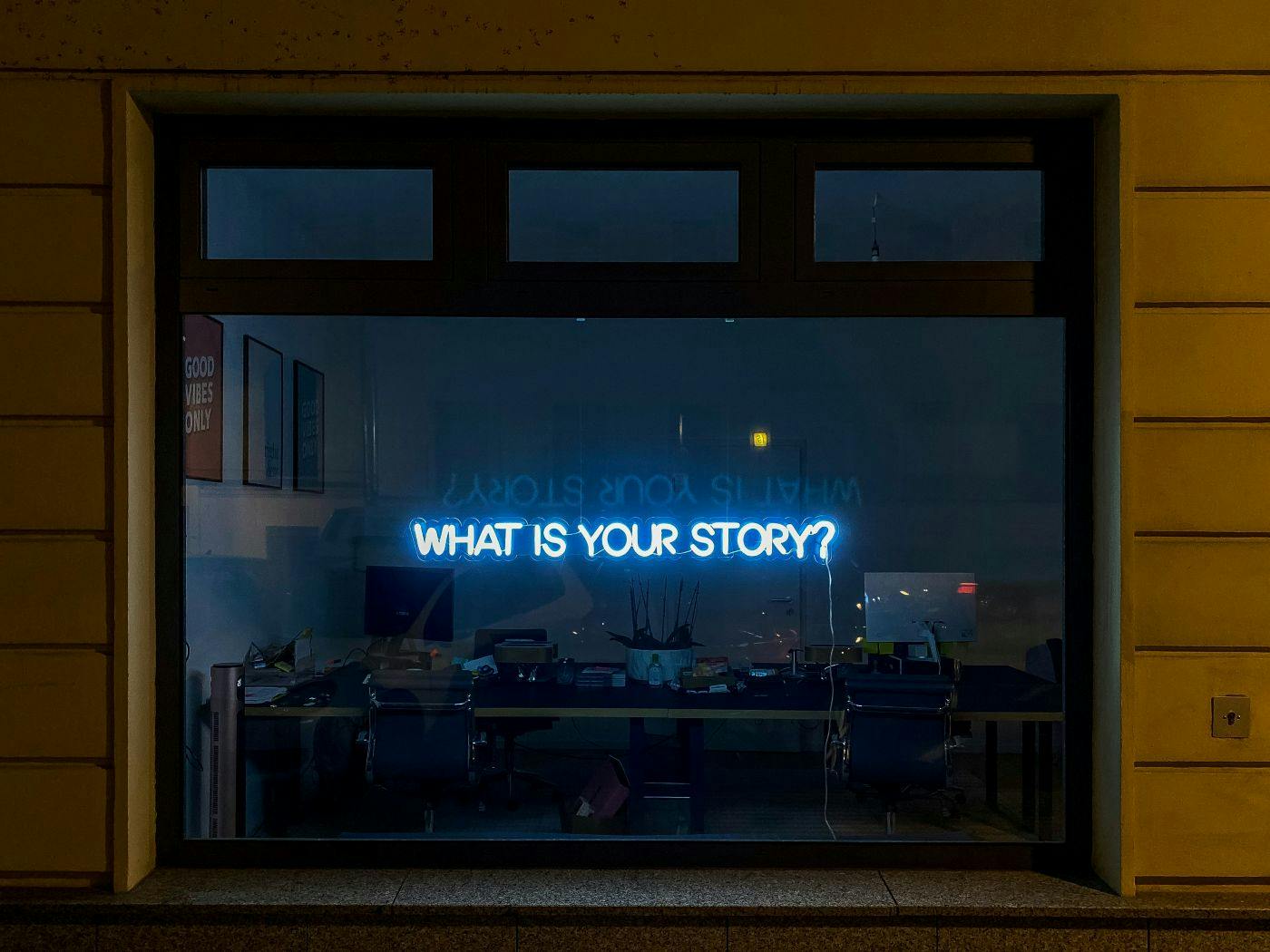 A blue neon light in a shop window reading What's Your Story