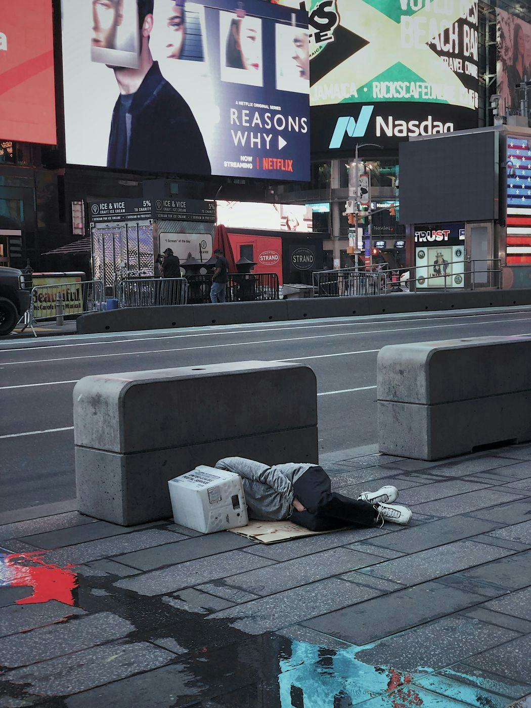 A person sleeping on the street in Times Square with their head in a Postal Carton