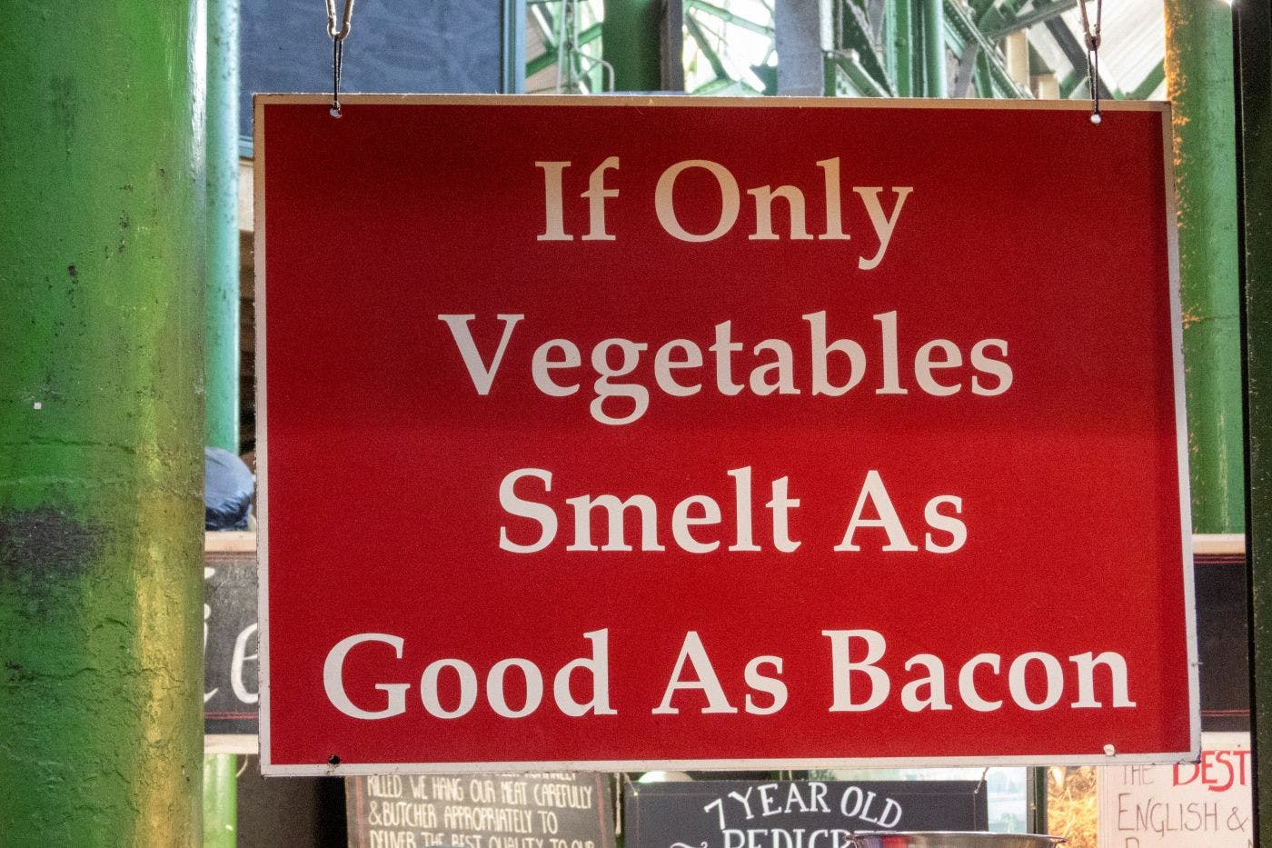 A red sign in a shop window reading, If Only Vegetables Smelt As Good As Bacon
