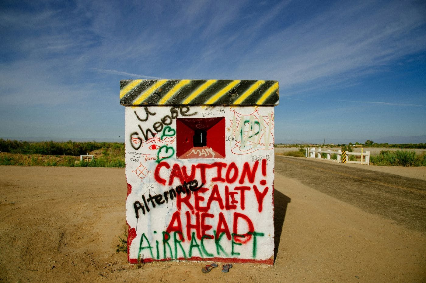 A graffitied guard shack with Caution Reality Ahead in red