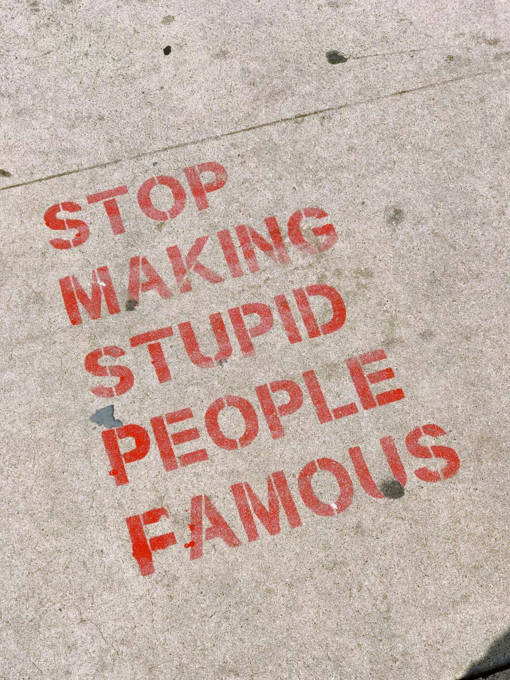 Stop Making Stupid People Famous in red stenciled on a sidewalk