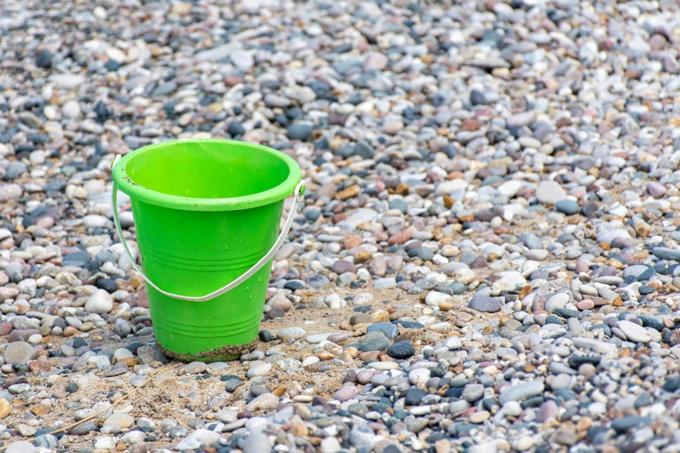 A green plastic bucket on the stones on a beach