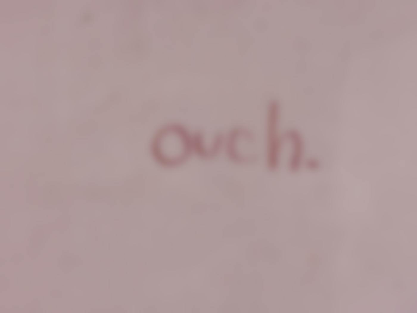 A pinkish wall with the word ouch written on it in red lipstick