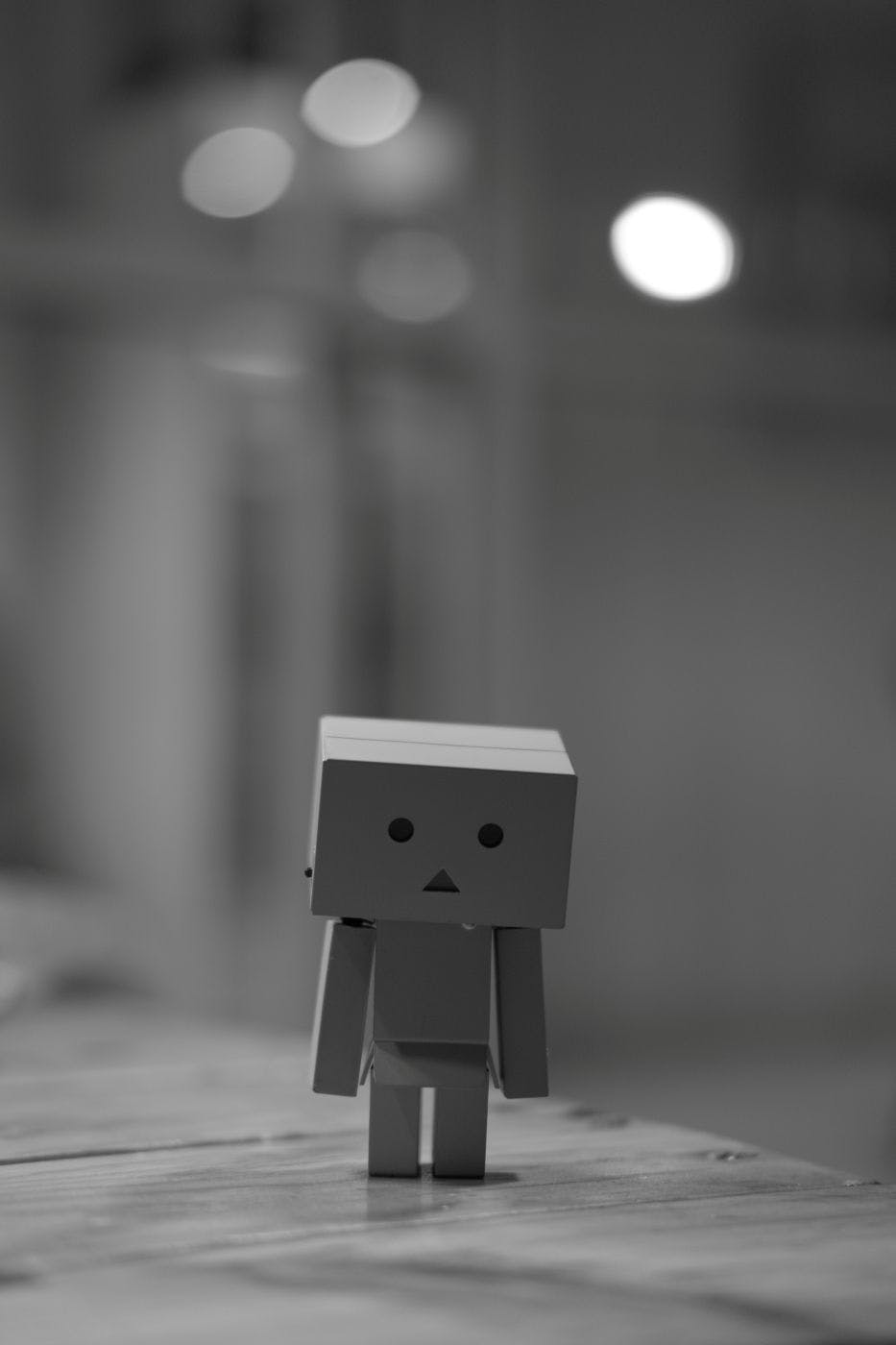 Grayscale of a sad little box robot standing on a table