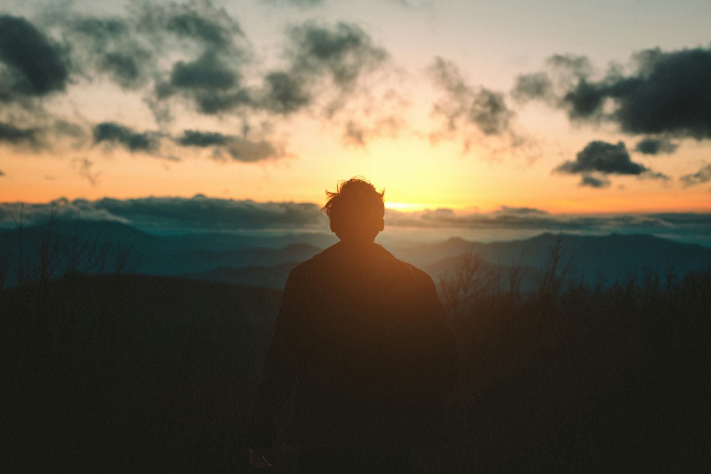 A person sitting on a hill, back to the camera, contemplating the sunset
