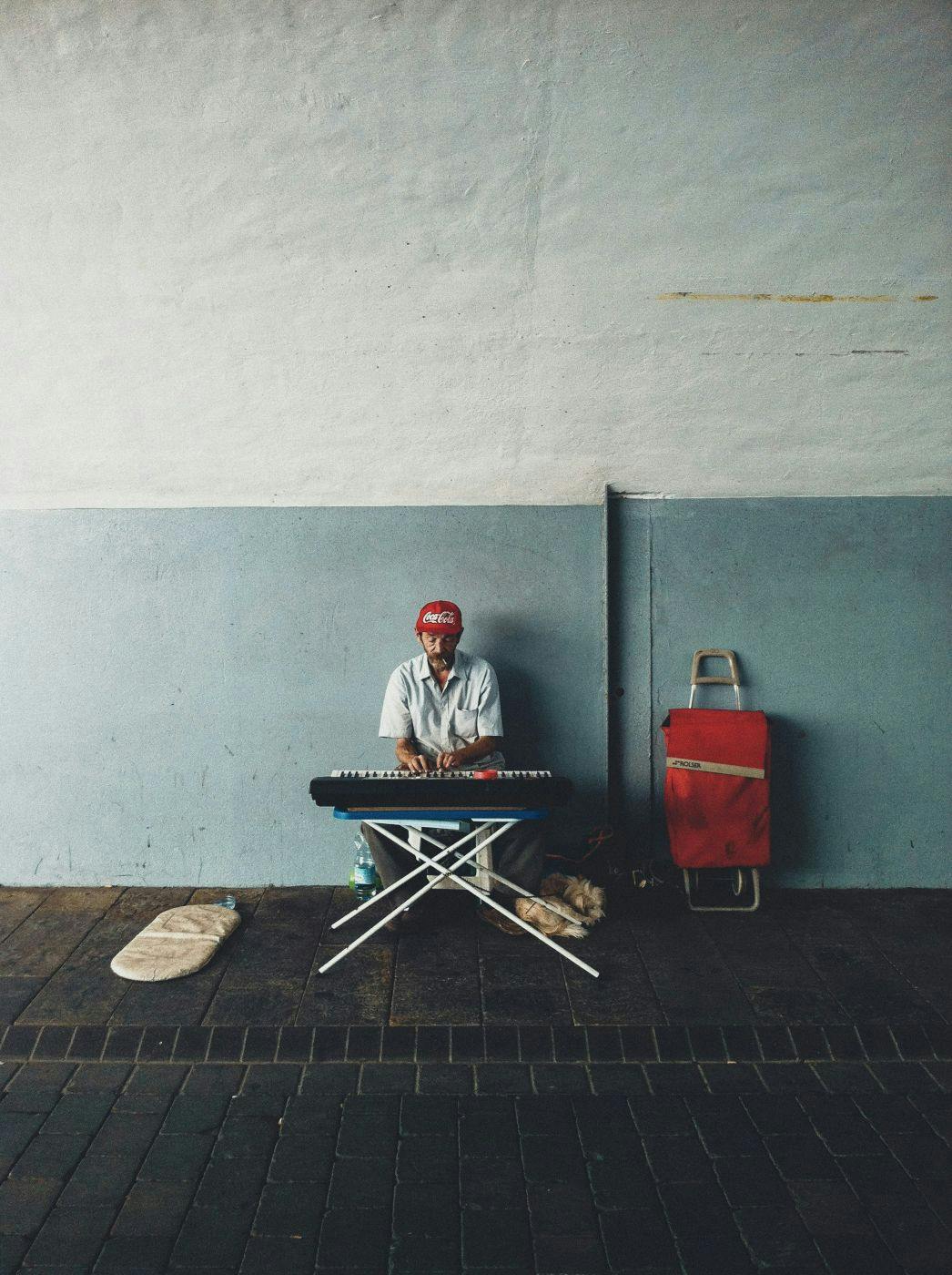 An older gent in a Coca-Cola hat playing electric piano on the street