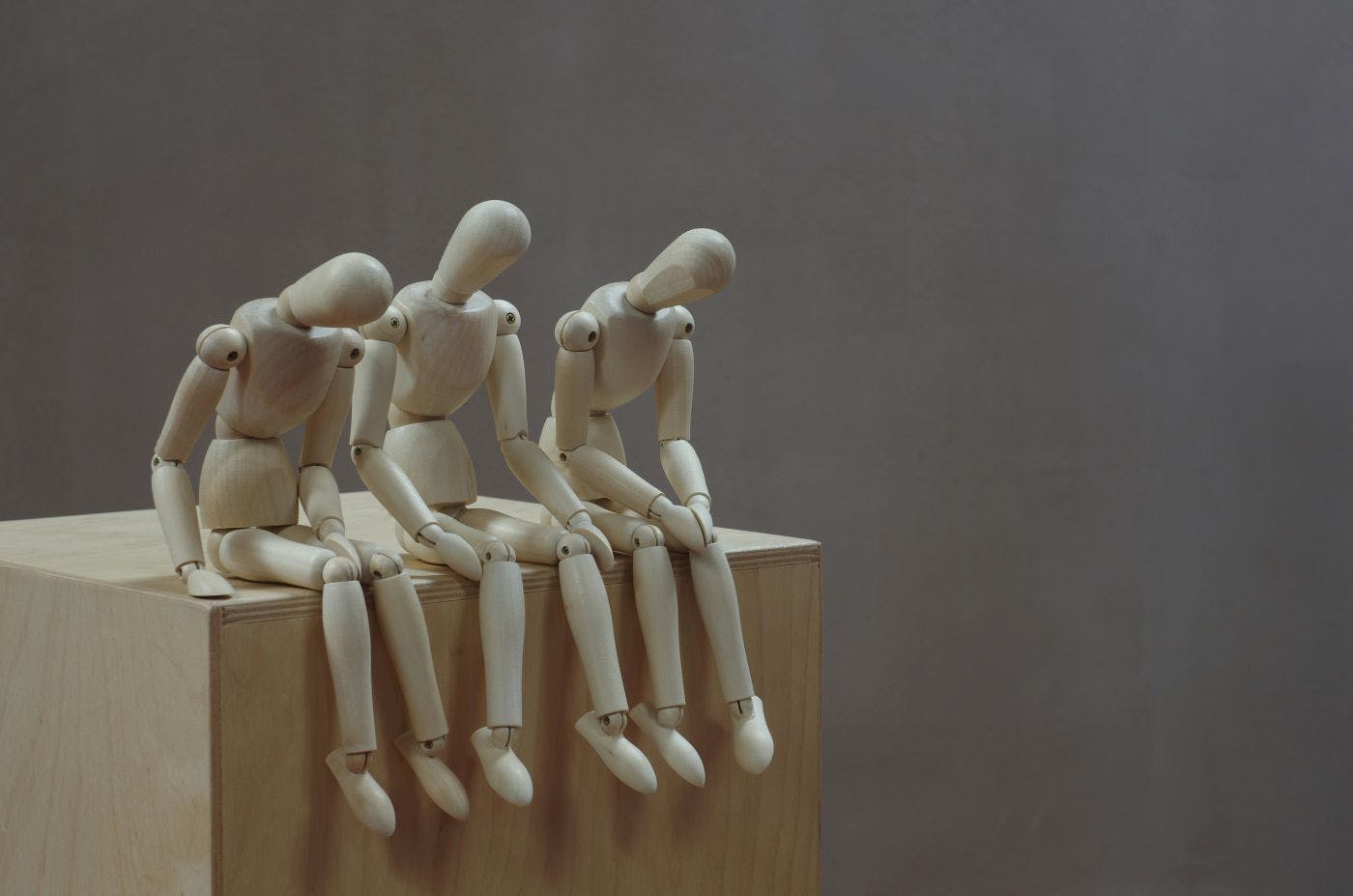 Three artist's mannequins sitting on a box looking very dejected