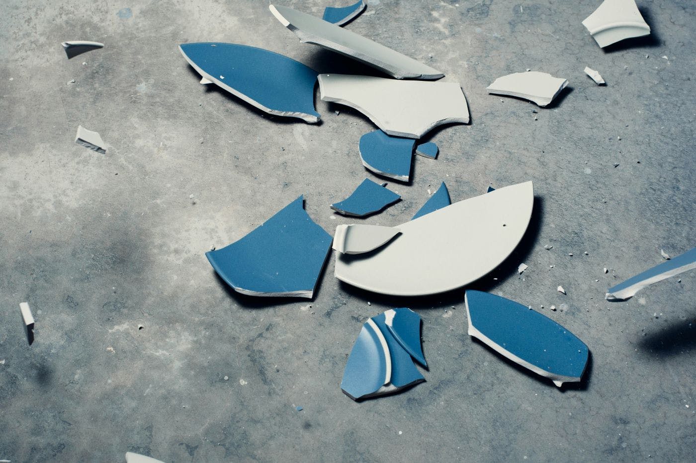 A shattered blue and white plate on a concrete floor