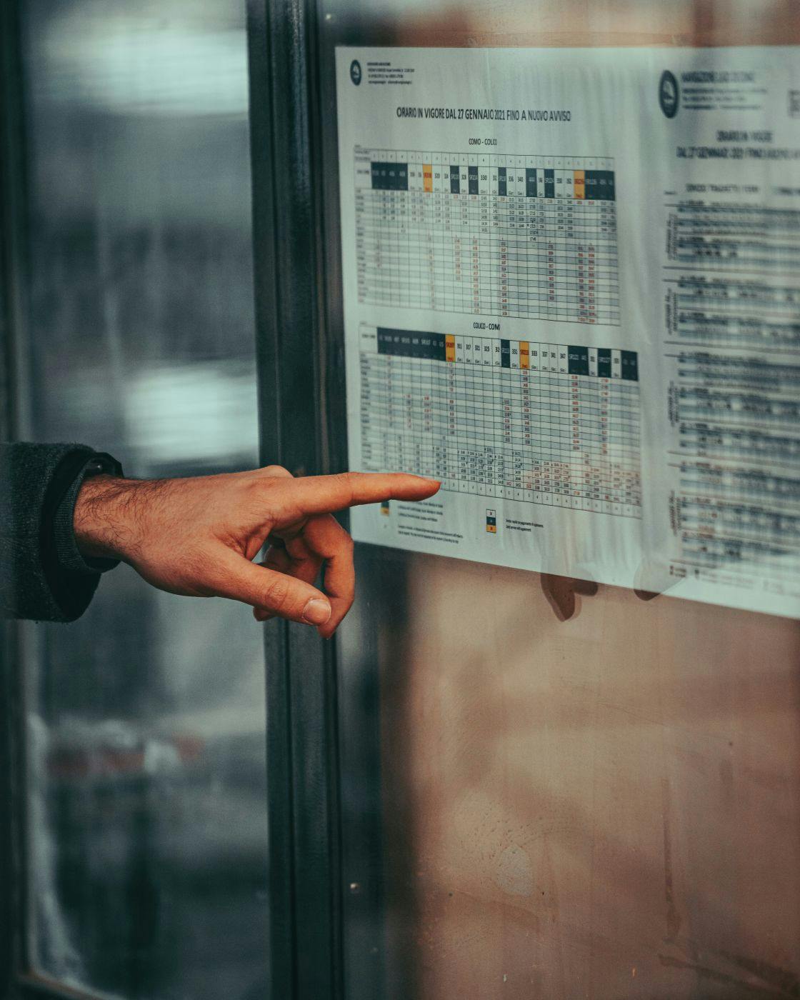 A man's hand pointing at a bus schedule