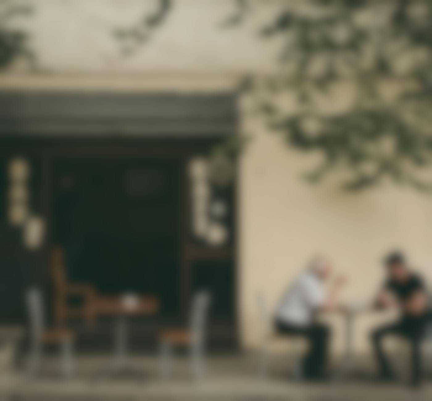 Two men having a conversation at a table outside a cafe