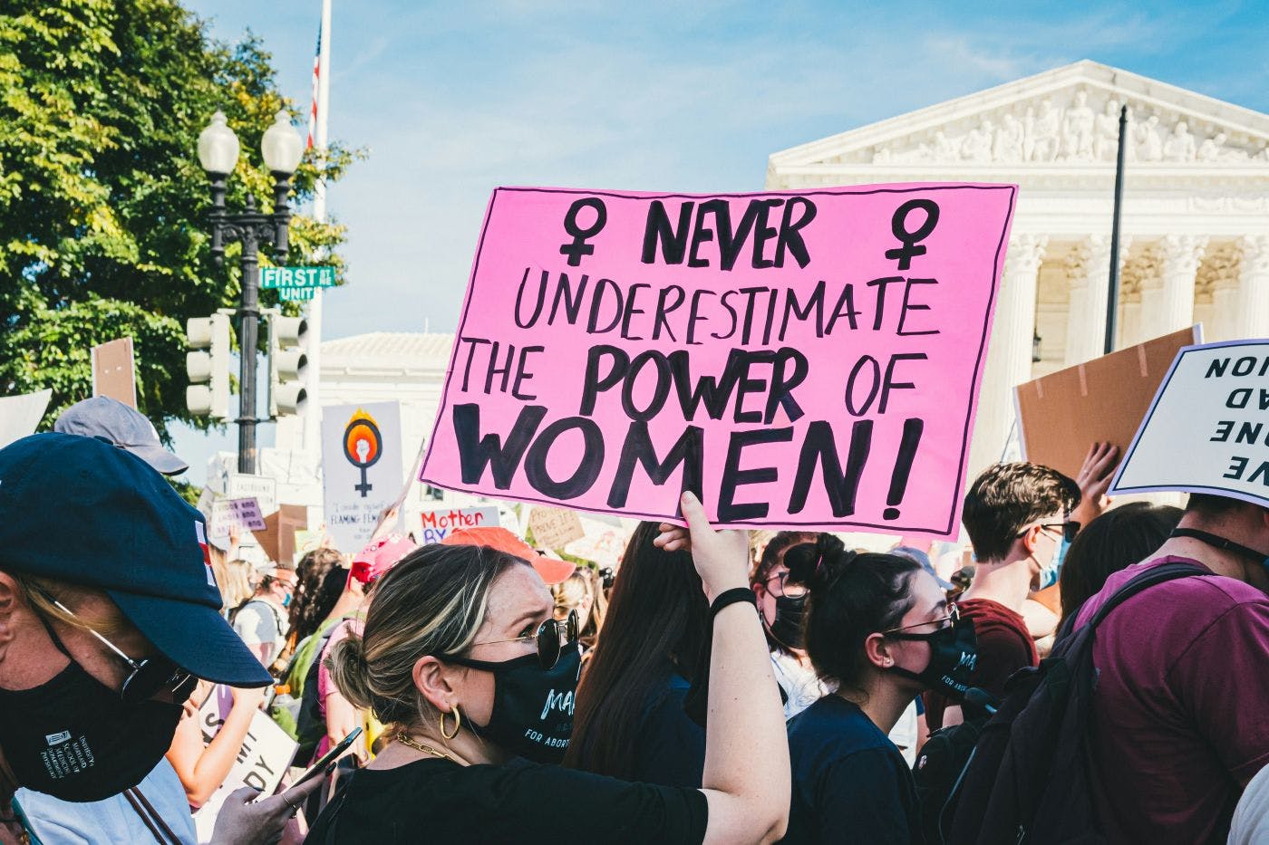 A woman at a rally holding a pink sign reading: Never underestimate the Power of Women